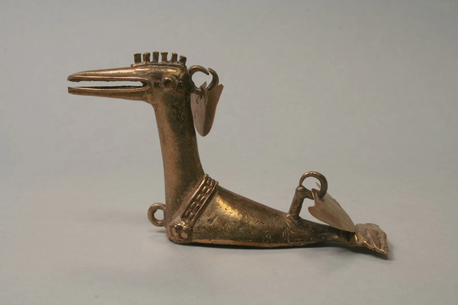 Colgante de oro en forma de ave, orfebrería quimbaya temprana, sobre fondo oscuro.