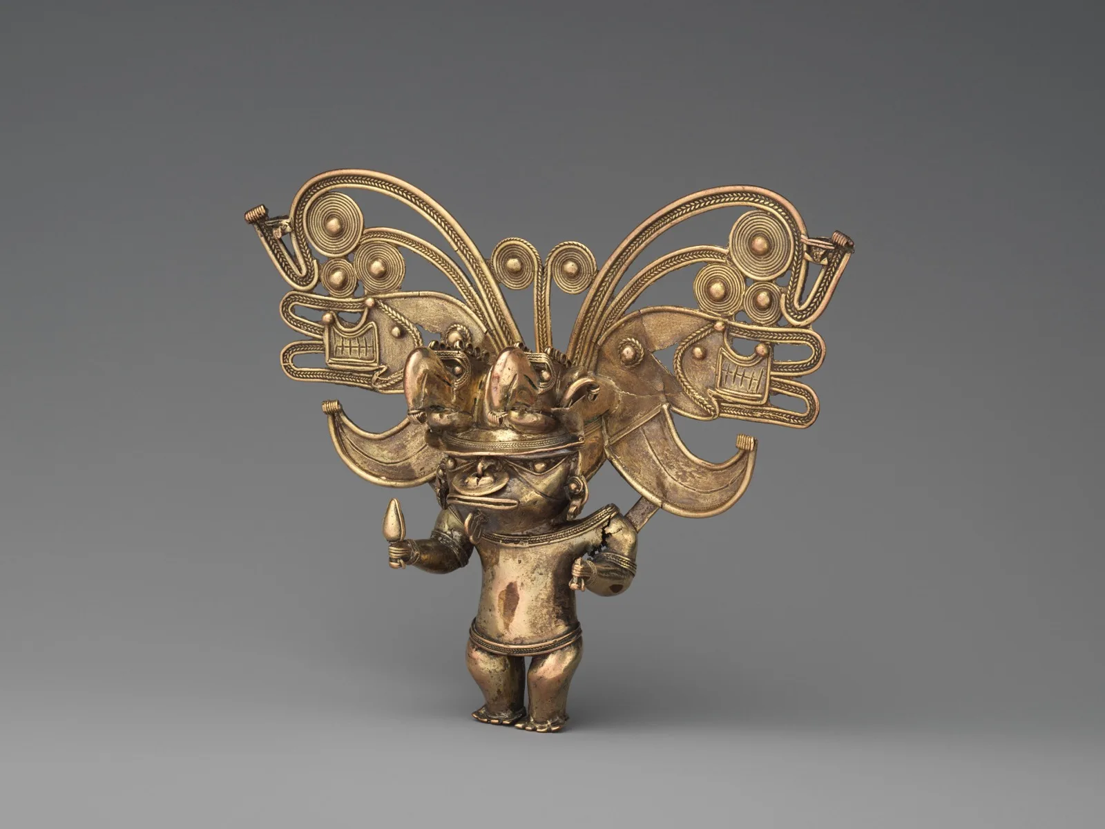 Colgante tairona de oro que representa una figura antropozoomorfa, sobre fondo oscuro.